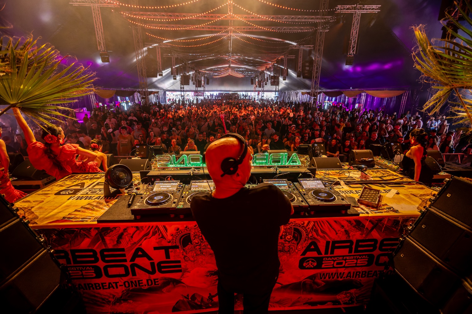 DJ STBAN performing an Afro-Tribal House set on stage at a festival, with dancers and the AIRBEAT ONE logo visible on the DJ booth.